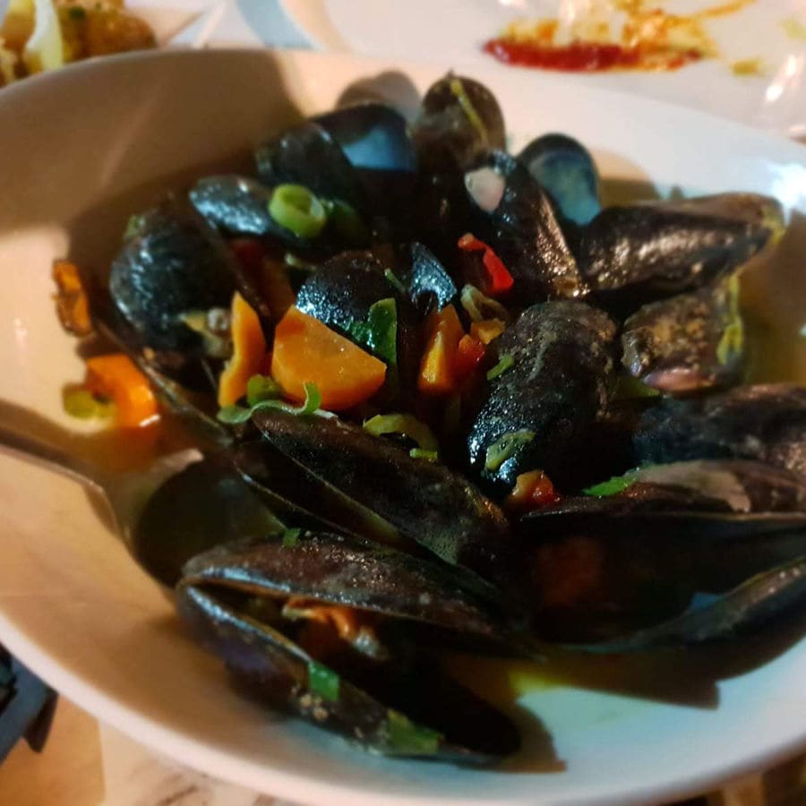 A plate of midia, small and flavorful Mediterranean mussels, is captured in a picture. The glossy shells reveal succulent meat inside, inviting a taste of the sea.